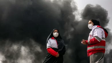 Mujeres de la Sociedad de la Media Luna Roja de Irán cerca de las columnas de humo de un incendio tras un ataque aéreo nocturno contra la refinería de petróleo de Shahran