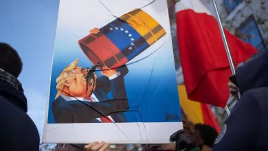 Un manifestante sostiene una pancarta con una caricatura de Donald Trump bebiendo petróleo venezolano